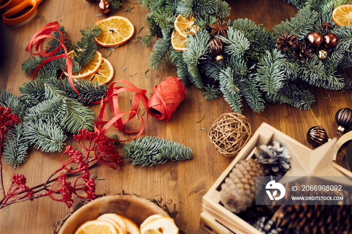 Workplace for Christmas wreath making: close-up of decorative paper ribbon, berry twig, coniferous branches and balls on table