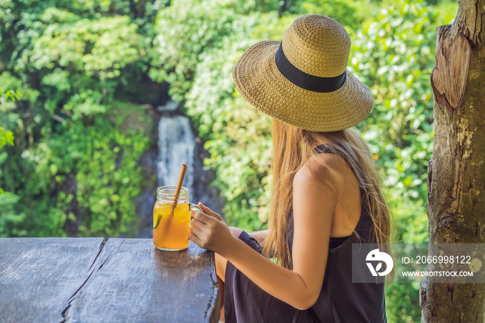 Closeup portrait image of a beautiful woman drinking ice tea with feeling happy in green nature and waterfall garden background