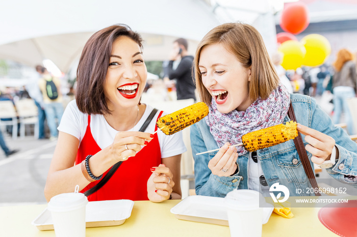 Woman friends eating street food corn at fastfood festival