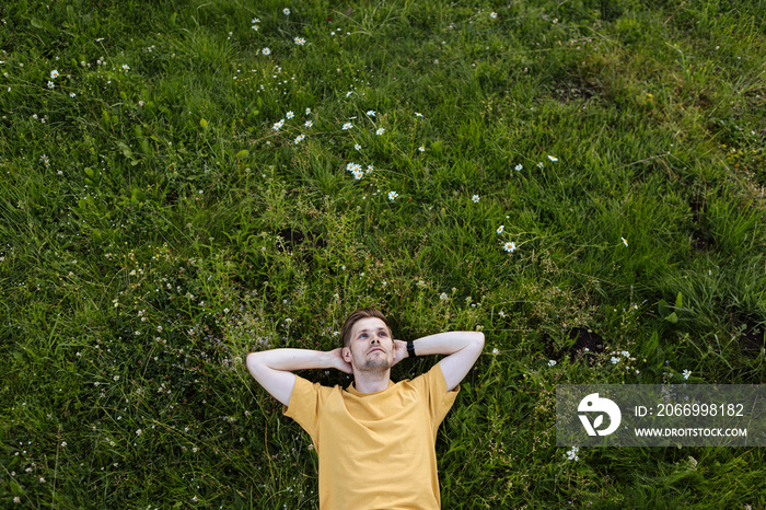 Young man laying in green grass with flowers. People fatigue from heat wave. Summer sleeping and relaxation techniques. Vitamin D sunbathing. Man power nap with eye closed. Rest after work