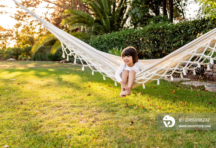 Cute little barefoot toddler boy relaxing in hammock in backyard garden. Child summer holidays healthy lifestyle and outdoors leisure activity. Vacation at home