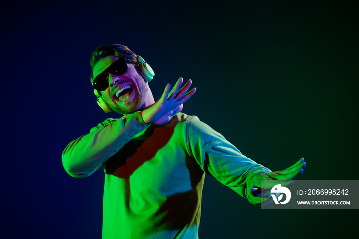 Photo portrait young man in sunglass listening music in earphones dancing happy isolated dark blue color background