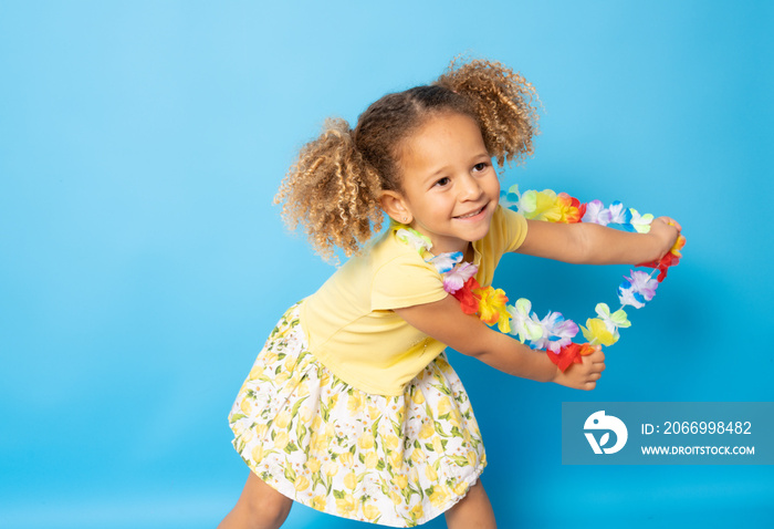 Happy little girl wearing Hawaiian necklace dancing isolated over blue background.