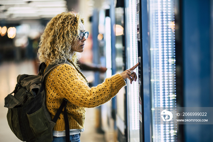 Alone traveler caucasian beautiful woman at the airport or. station choosing and buying food from automatic machine - concept of travel lifestyle for independent people enjoying life