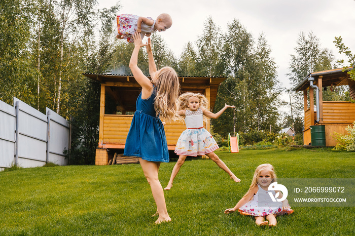 Happy kids and mother playing in garden on grass. Summer time.