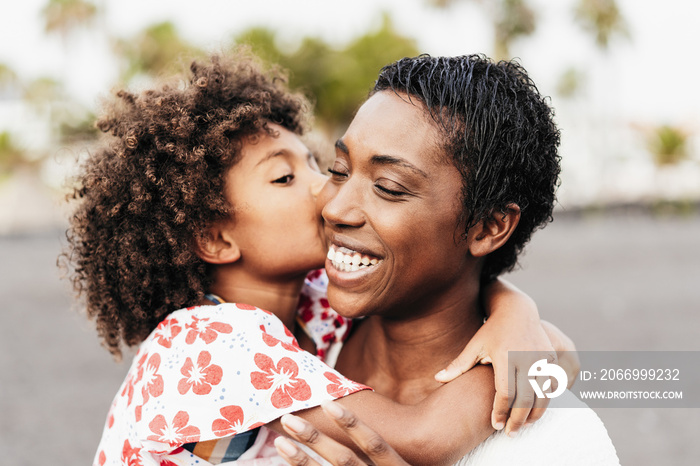 Happy black mother having tender moment with her child at the beach summer day - Focus on mother face