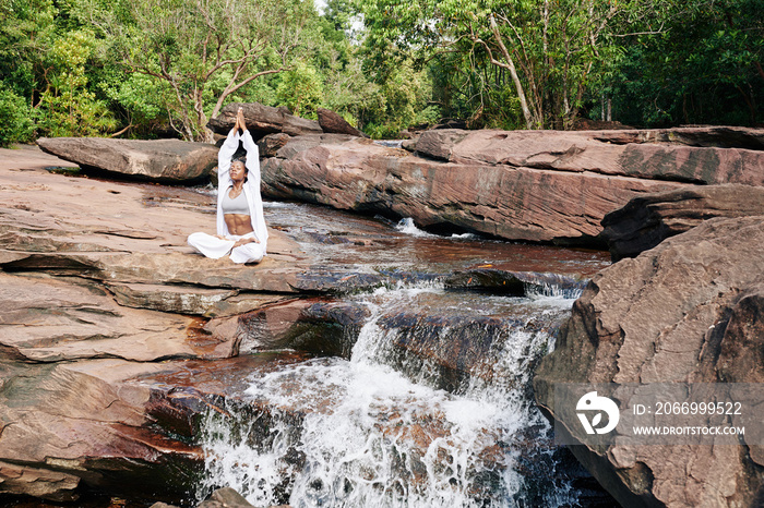 Beautiful young woman sitting by waterfall and enjoying meditation in nature