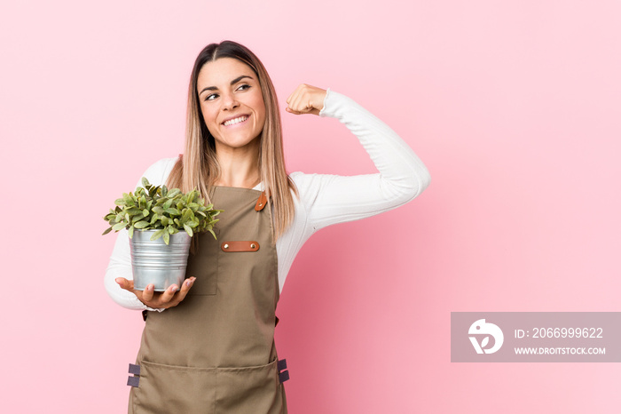 Young gardener woman holding a plant raising fist after a victory, winner concept.