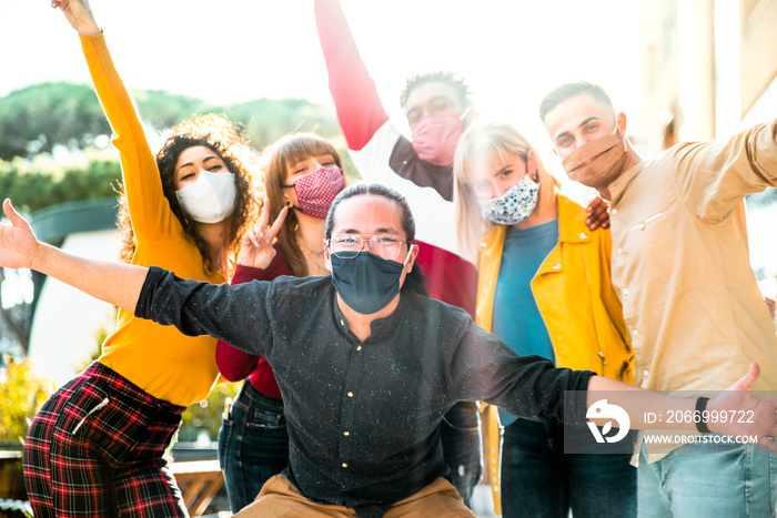 Group of multiracial people wearing protective face masks smiling at camera - New normal friendship concept with multicultural friends having fun outdoor - Focus on asian guy