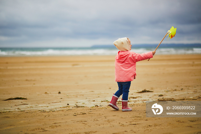 Adorable toddler girl playing with pinwheel on the sand beach at Atlantic coast of Brittany, France