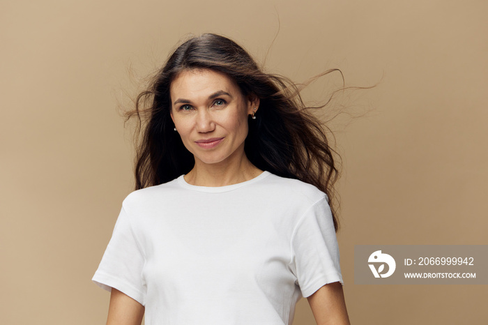 portrait of a beautiful attractive woman with long, beautiful, well-groomed hair blowing in the wind, stands smiling cutely at the camera on a beige background.