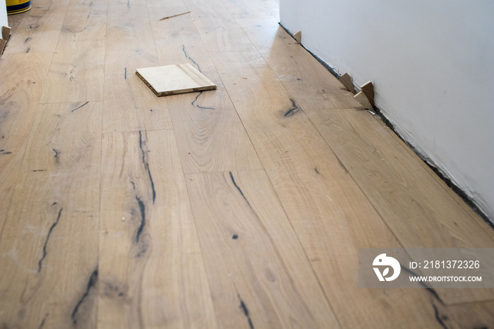 installation of parquet boards during the renovation of an apartment, piece of oak board on the newly assembled floor near a white wall