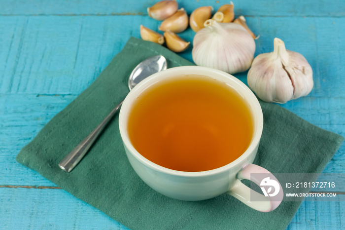 Garlic tea in ceramic cup with garlic on blue wooden background.