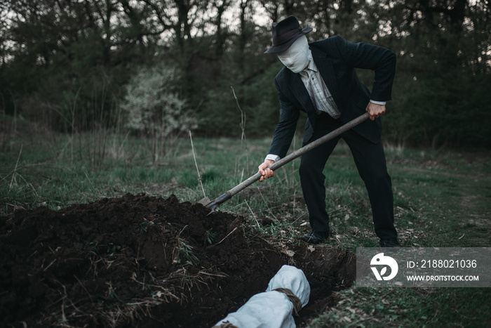 Bloody murderer is digging a grave for the victim