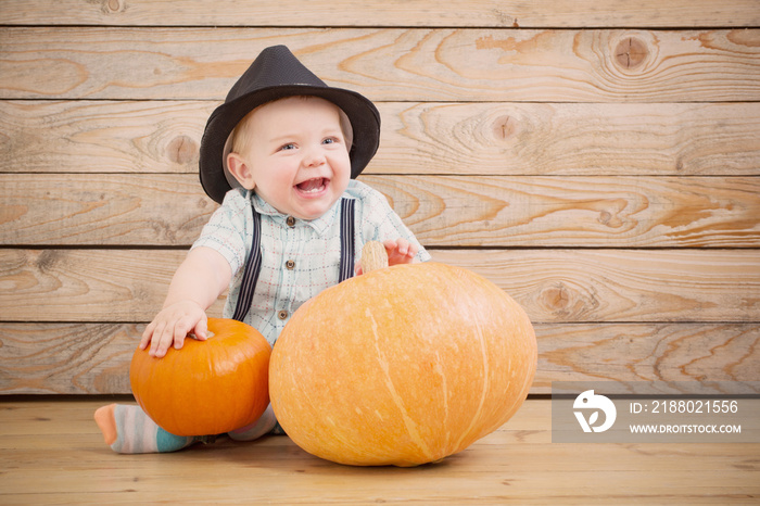 baby in black hat with pumpkins on wooden background