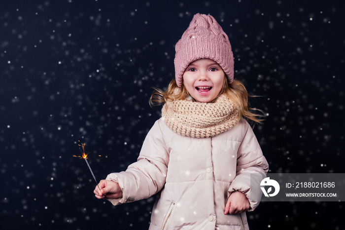 charming little girl in a knitted pink hat holding fireworks on black background in a studio.Cute bl