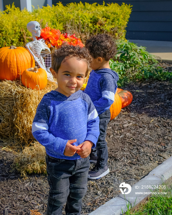 African-American twin toddlers playing in front of their house with Halloween decorations; one tween