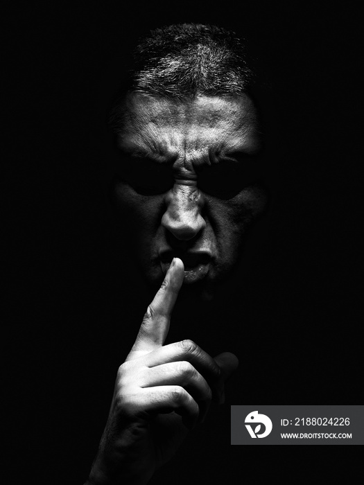 Furious mature man with an aggressive look making the silence sign in a violent and threatening way.
