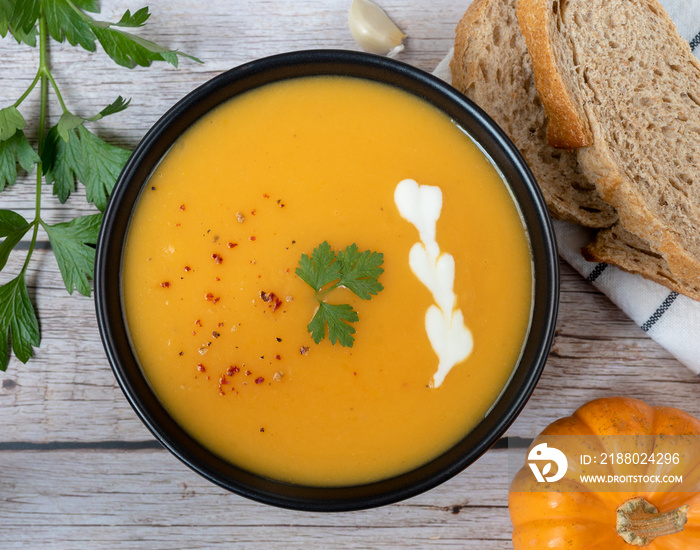 Autumn pumpkin soup and ingredients on a wooden table.