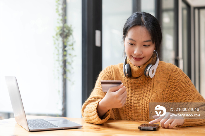 Attractive  Asian female sits at her desk, holding a smartphone and a credit card. close-up image. O