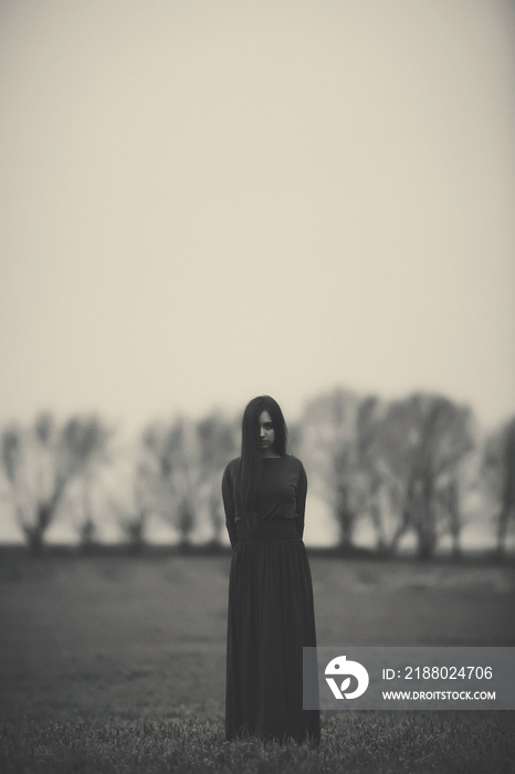 Girl in a long dress on the background of a gloomy forest black and white photo . A woman in a dark 