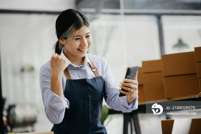 Woman who runs an online store with a happy face is holding her phone to check sales, she sells onli