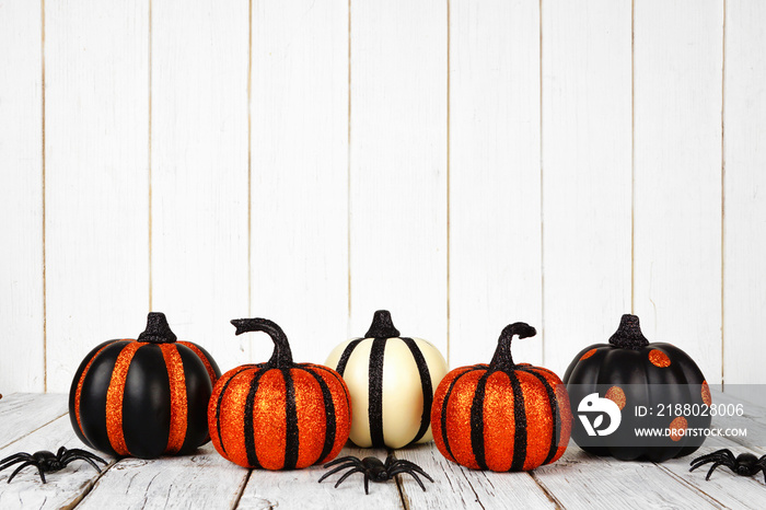 Black and orange glittery Halloween pumpkins against a white wood background