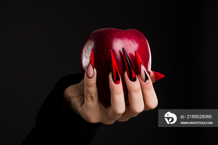 Hands with scary nails manicure holding  poisoned red apple , isolated on black background