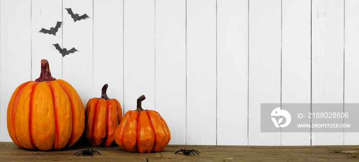 Halloween pumpkin decor on a wood shelf against a white wood panel wall with bats. Banner with copy 