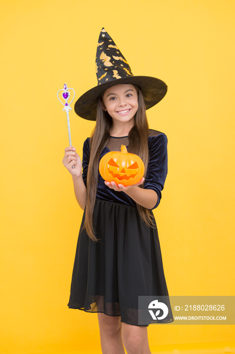 happy girl wear witch hat holding magic wand and pumpkin jack o lantern to create enchantment on hal