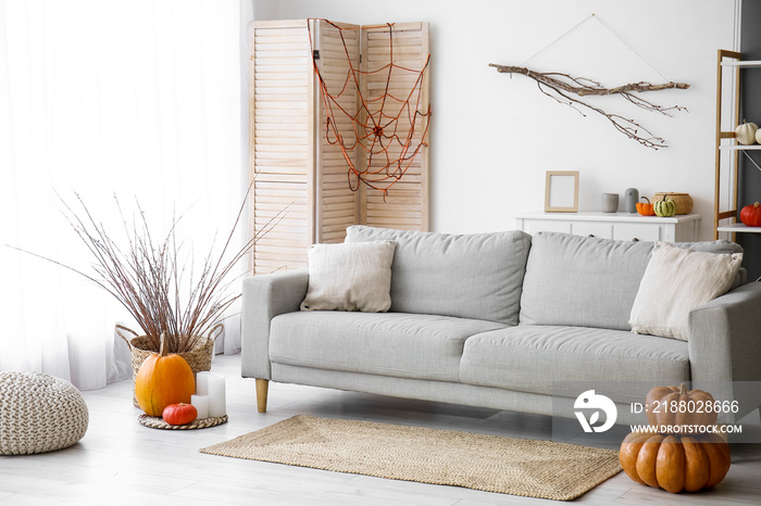 Interior of light living room with grey sofa, Halloween pumpkins and tree branches