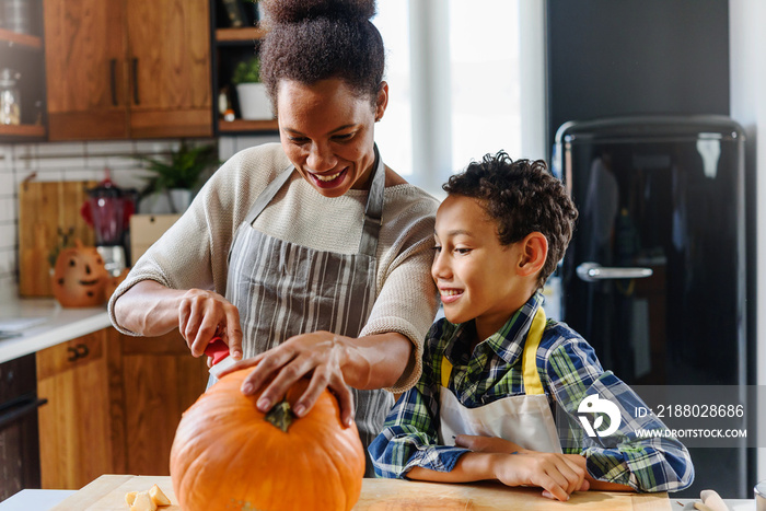 Young woman with her little son are preparing for Halloween on kitchen. Mother with son are having f