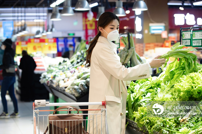 戴口罩的青年女人在超市挑选青菜