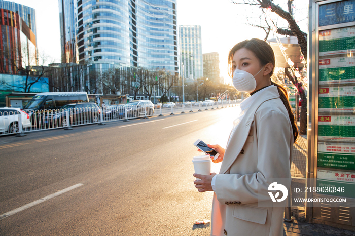 戴口罩的年轻女人站在公交车站