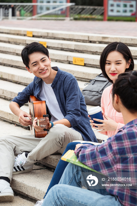 年轻的大学生坐在台阶上弹吉他唱歌