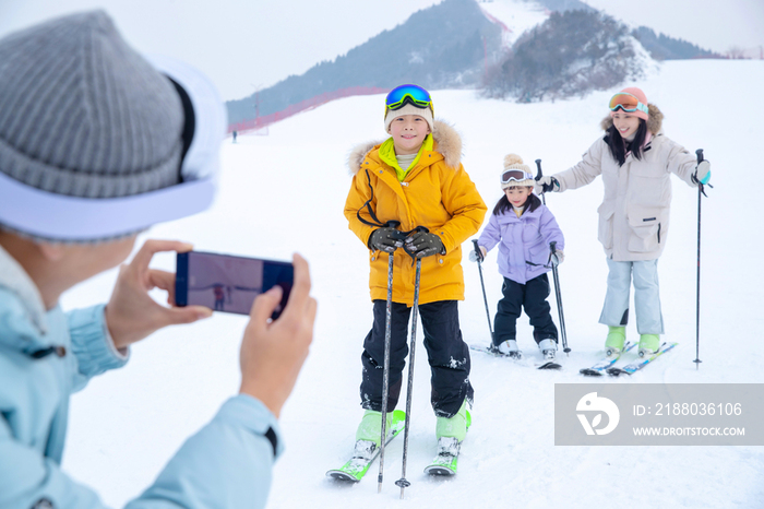 滑雪场上父亲用手机给孩子们和妻子拍照