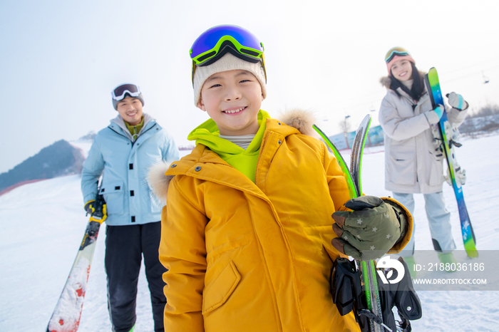 雪场上拿着滑雪板的一家三口