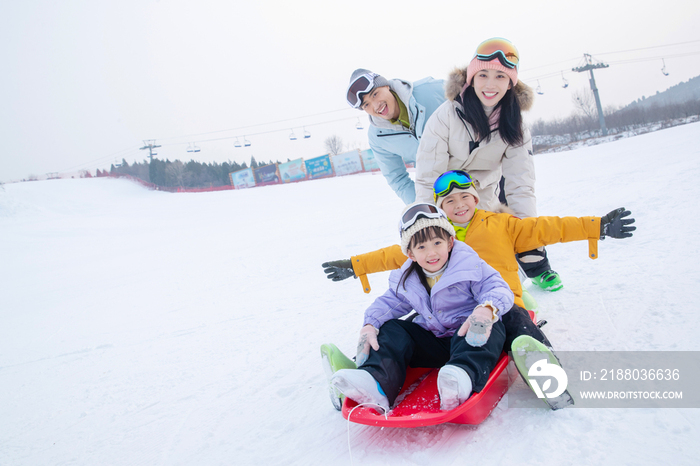 滑雪场上父母推着坐在雪上滑板的孩子们