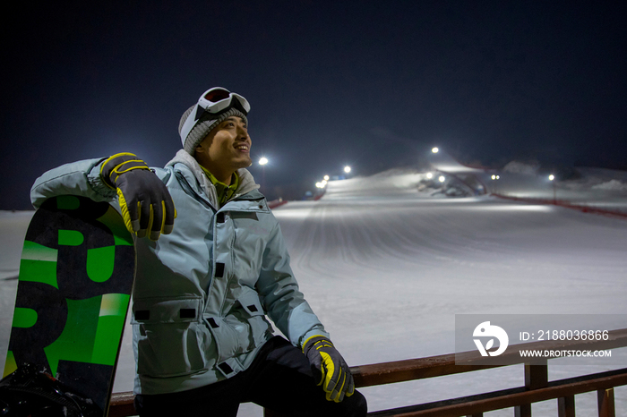 夜晚青年男人坐在滑雪场内的护栏上