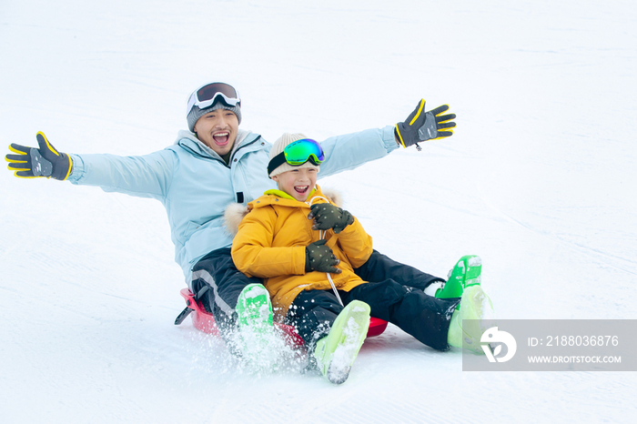 快乐父子坐着雪上滑板滑雪