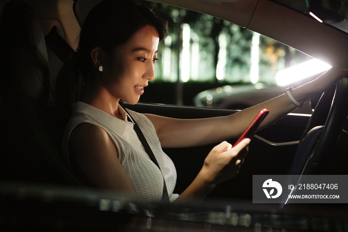 夜晚青年女人坐在汽车里使用手机
