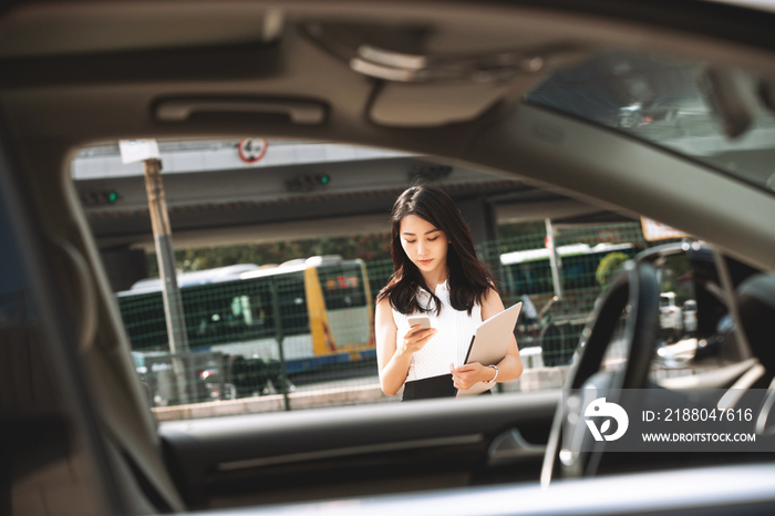 低头使用手机的青年女人走向汽车