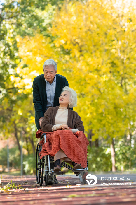 老年男人推着坐轮椅的老伴散步
