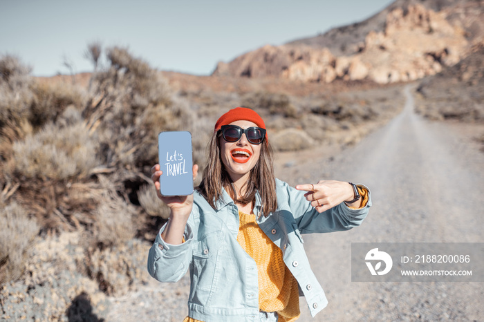 Young and happy woman showing smartphone with a drawing on a topic of travel during a trip on the desert road