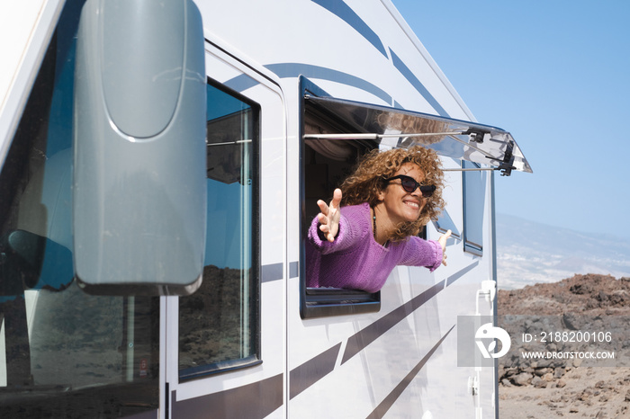 Portrait of beautiful smiling curly woman wearing glasses and violet sweater traveling in motorhome camper looking out the window happy. Caucasian woman enjoying free lifestyle, vacation, travel
