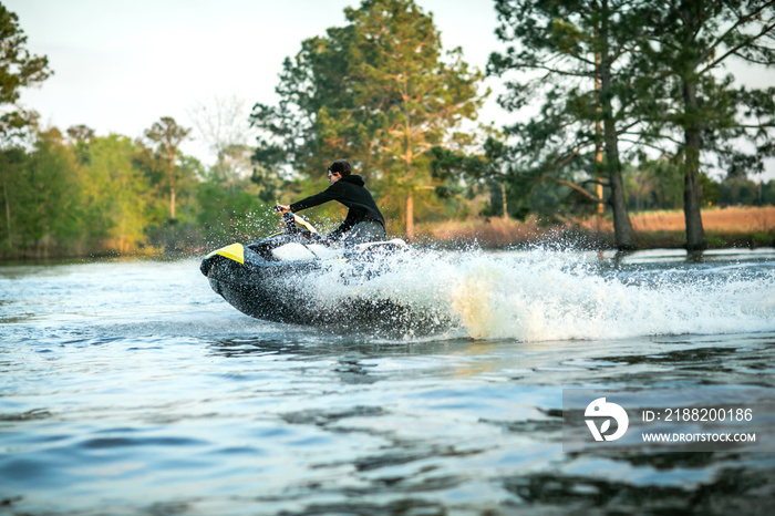 Teenage boy man driving a personal watercraft outside on a lake pond at sunset