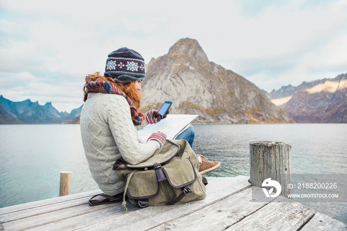 Woman traveler with a backpack sitting on a wooden pier.