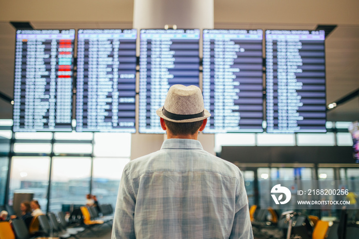 Solo traveler - man standing inside airport terminal looking at a schedule.  Travel and transportation themed image.