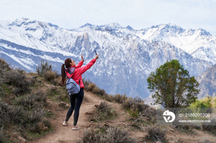 young red haired woman with red jacket and backpack, in a video call with her phone in the middle of the Andes mountains of Chile