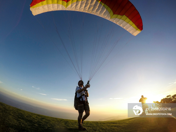 Paragliding man training on mountain top at sunset